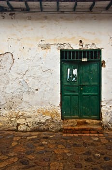 An old weathered colonial wall with a green door in Villa de Leyva, Colombia.