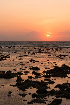 Warm tropical sunset over Agung volcano, the highest mountaint on Bali island, Indonesia with sea and stones on front