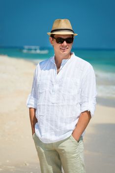 Carefree happy young man in sunglasses and hat on the sunny coast with the blue sea and boat on background
