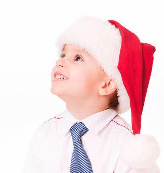 Happy little boy in shirt and tie in santa hat looks up. Isolated on white.
