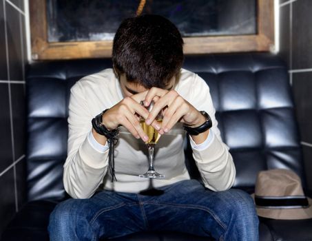 sad man with glass of wine on sofa in night club