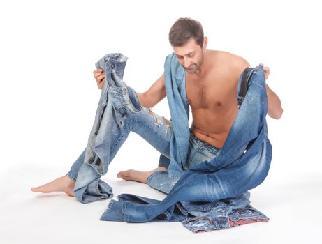 Cool shirtless trendy man in a pair of modern ragged jeans sitting deciding what to wear 