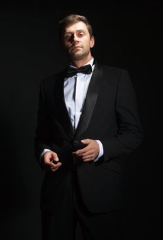 Dramatic portrait of a suave handsome man in a tuxedo and bowtie highlighted in darkness