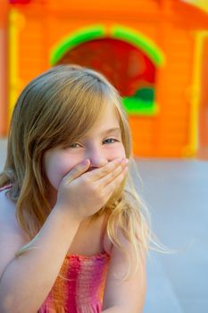 Blond kid girl funny gesture hand in mouth in playground with sundress