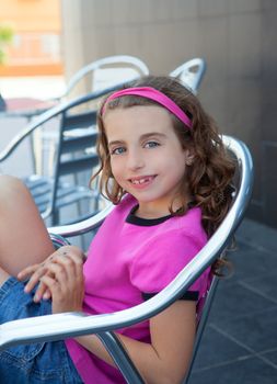 Smiling girl sitting in outdoor aluminium silver chair and pink t-shirt