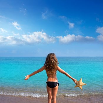 blue beach kid girl with bikini holding starfish looking sea in rear view