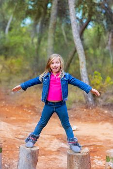 kid girl climbing tree trunks with open arms having fun in the pine forest