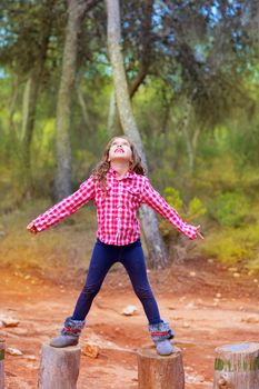 kid girl climbing tree trunks with open arms having fun in the pine forest