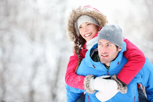 Happy winter travel couple. Man giving woman piggyback ride on winter vacation in snowy forest. Young interracial couple, Asian woman, Caucasian man.