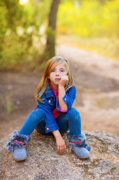 blond kid girl pensive bored expression in the forest outdoor sitting on a rock