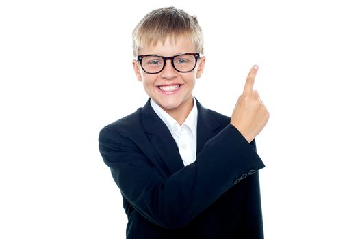 An adorable young boy in formals pointing towards copyspace area