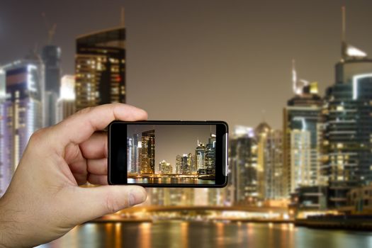 Hand and cellphone with modern buildings in Dubai