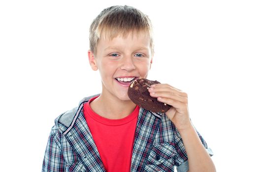 Fashionable young boy eating chocolate cookie and smiling while facing camera