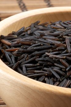 Wood Bowl with Perfect Wild Brown Rice closeup on Straw mat background