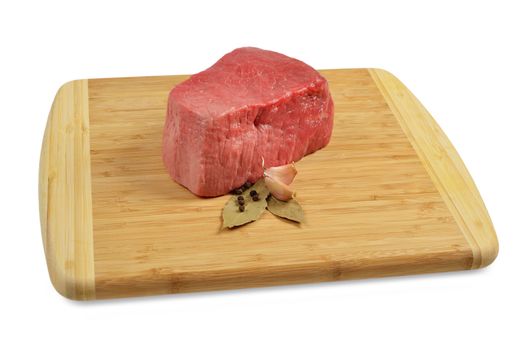 Piece of raw beef on a wooden board, decorated with garlic and bay leaves.