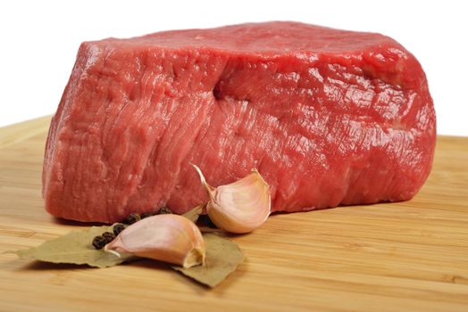 Piece of raw beef on a wooden board, decorated with garlic and bay leaves.