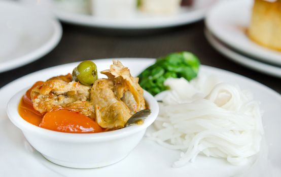 Red curry with roast duck served with vegetable  and rice vermicelli on white plate