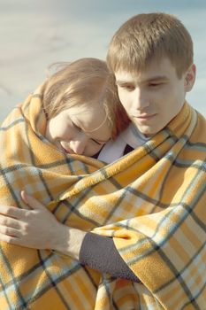 Young beautiful couple in winter wrapped in a yellow blanket