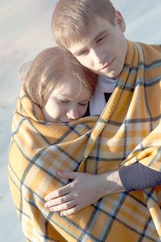 Young beautiful couple embracing in winter wrapped in a yellow blanket