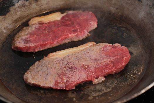 Beef steak cooking in a iron grill pan.