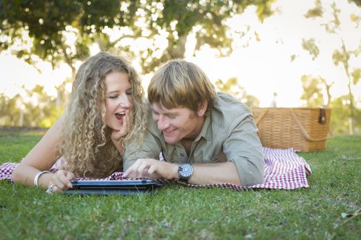 Playful Loving Couple Using a Touch Pad Computer at Their Picnic Outside.