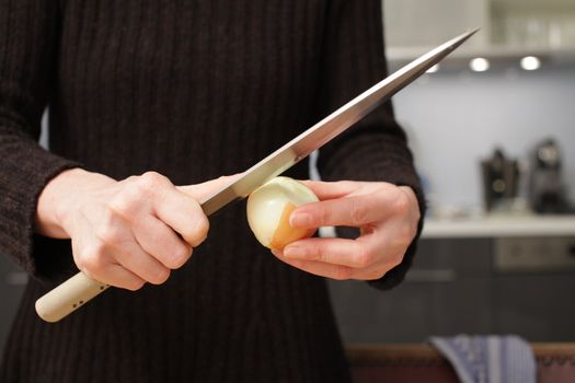 Freshly washed white onion on cutting board with knife.