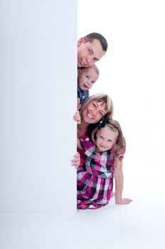 Happy smiling family looking out from behind the wall