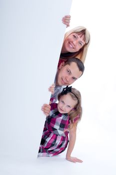 Happy smiling family looking out from behind the wall