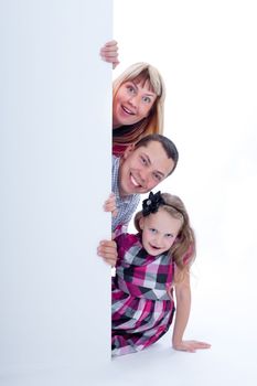 Happy smiling family with amazed facial expressions looking out from behind the wall