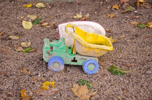 abandoned plastic truck toy in autumn sand box after rain 