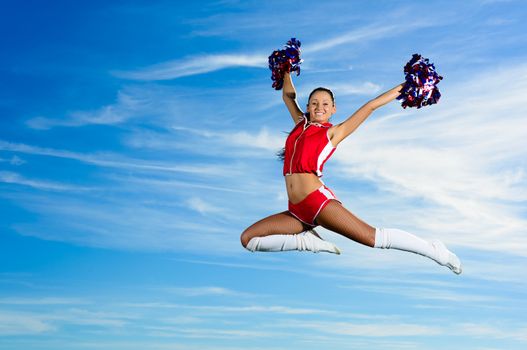 Young cheerleader in red costume jumping against blue sky