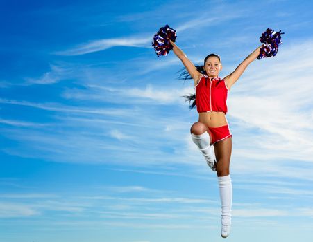 Young cheerleader in red costume jumping against blue sky