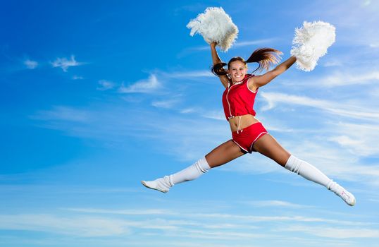 Young cheerleader in red costume jumping against blue sky