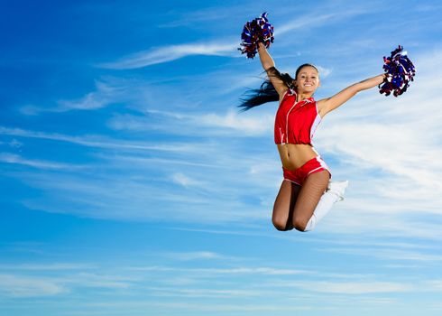 Young cheerleader in red costume jumping against blue sky