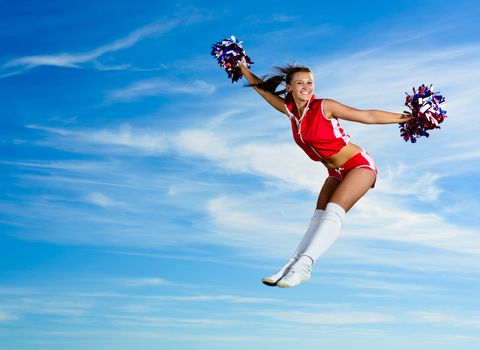 Young cheerleader in red costume jumping against blue sky