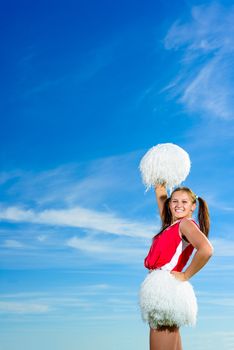 Young cheerleader in red costume with pampon against blue sky