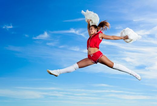 Young cheerleader in red costume jumping against blue sky