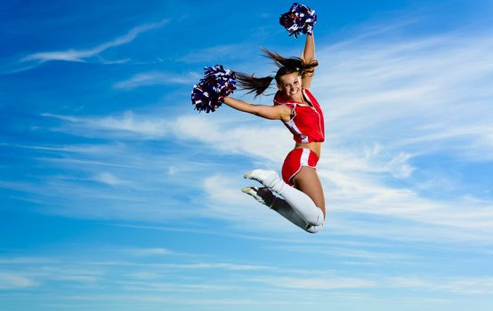 Young cheerleader in red costume jumping against blue sky