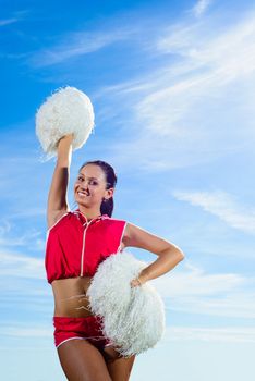 Young cheerleader in red costume with pampon against blue sky