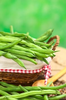 Fresh raw green beans in basket with green background (Selective Focus, Focus on the beans in the middle of the image)