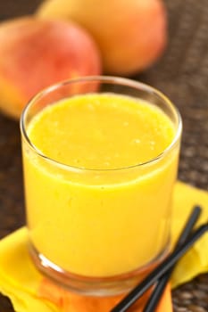 Fresh homemade mango juice in glass with straws on the side and mango fruits in the back (Selective Focus, Focus on the front rim of the glass)