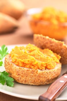 Sweet potato spread on wholegrain bun on plate with knife (Selective Focus, Focus on the front of the spread) 