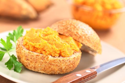 Sweet potato spread on wholegrain bun on plate with knife (Selective Focus, Focus on the front of the spread) 