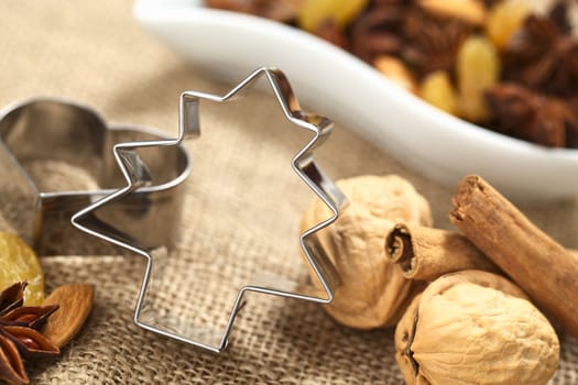 Christmas tree cookie cutter with other baking ingredients (walnut, cinnamon, anise, raisin and almond) (Selective Focus, Focus on the upper part and right side of the cookie cutter) 