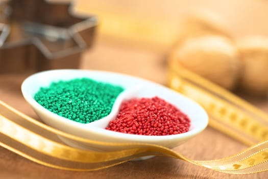 Red and green colored sugar sprinkles used for decorating Christmas cookies with golden ribbon around, walnuts and cookie cutter in the back (Selective Focus, Focus one third into the red sprinkles)