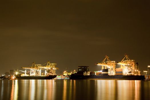 Big Container Cargo freight ship with working crane in shipyard at night for Logistic Import Export background
