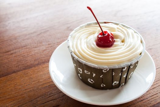 Cupcake with red cherry on white plate