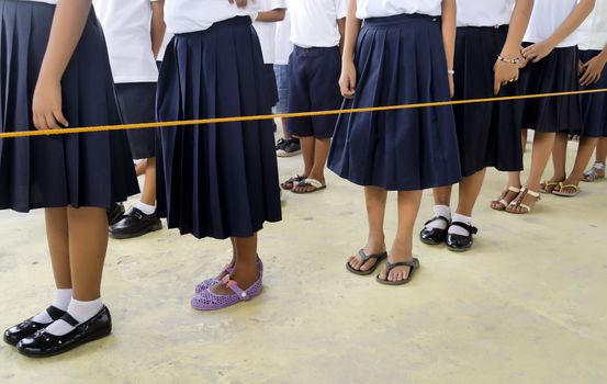 Students in school uniform standing in line inside an orange nylon cord