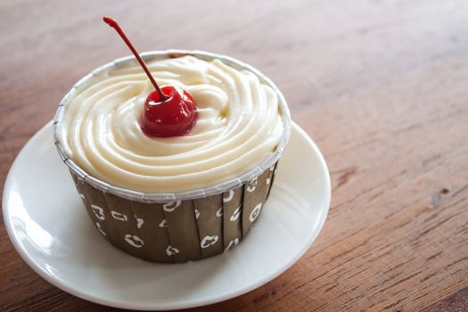 Cupcake with red cherry on white plate