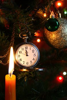 Vintage pocket watch hanging on Christmas tree near lighting candle